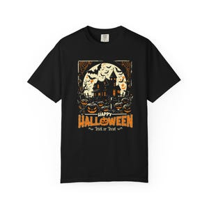 May include: A black short-sleeve t-shirt featuring a graphic print of a haunted house, a full moon, bats, and jack-o'-lanterns. The text reads Happy Halloween and Trick or Treat in orange and white lettering centered on the chest.