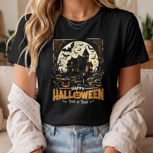 A person wearing a black t-shirt printed with a haunted house and jack-o-lanterns graphic under a full moon, with the text Happy Halloween Trick or Treat.