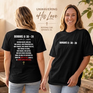 May include: A black t-shirt featuring white text on the front reading ROMANS 8:38-39. The back displays the full Bible verse text in white, with the words LOVE OF GOD and CHRIST JESUS OUR LORD highlighted in red, accompanied by a small cross icon.