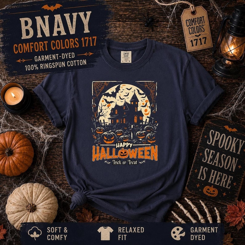 A navy blue t-shirt laid flat on wood with a haunted house and pumpkin graphic, styled with miniature pumpkins and a lantern.