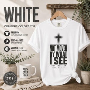 May include: A white short-sleeve t-shirt featuring a black graphic of a cross and the text "NOT MOVED BY WHAT I SEE FAITH NOT SIGHT 2 CORINTHIANS 5:7". The shirt is made of 100% ringspun cotton and has a soft-washed, vintage-style finish.