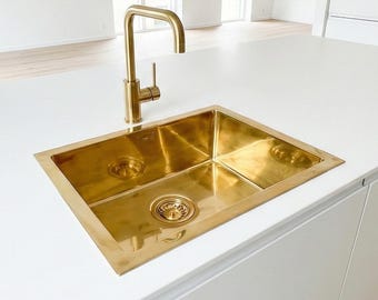 May include: A modern kitchen island with a gold-colored sink and faucet. The sink is rectangular and set into a white countertop. The faucet has a gooseneck design. The kitchen has white cabinets and light wood flooring.