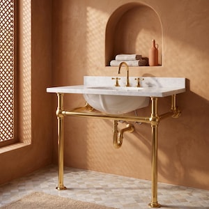 May include: A white porcelain sink basin set into a white marble countertop, supported by a polished gold metal pipe frame. The fixture includes a gold faucet with two handles and a matching gold P-trap drain pipe underneath the basin.