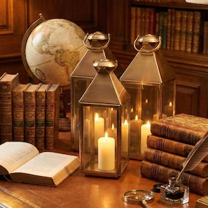 May include: A warm-toned image of a study with a globe, books, and lit lanterns. Three brass lanterns with lit candles sit on a leather desk. Books, a magnifying glass, and an inkwell complete the scene.