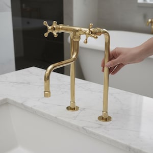 Pode incluir: Uma torneira de casa de banho dourada com puxadores em forma de cruz e um bico curvo. A torneira está montada numa bancada de mármore branco. O design é clássico e elegante, adequado para uma casa de banho de luxo.
