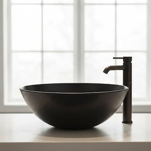 May include: A dark bronze, hammered-finish vessel sink with a matching faucet. The round sink sits on a light-colored countertop, with a window in the background. The faucet has a single-handle design.
