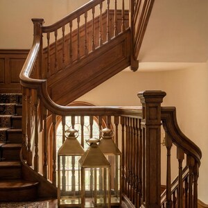 May include: A grand wooden staircase with a curved banister and balusters. Three gold lanterns with glass panels sit on the landing. A patterned rug covers the lower steps. A large arched window is visible.