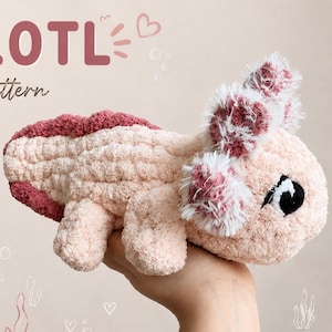 May include: A hand-knitted axolotl plushie in shades of pink, held in a hand. The plushie has a textured, chunky appearance with a dark pink dorsal fin and fluffy gills. The image includes text that reads "AXOLOTL Hand Knit Pattern".