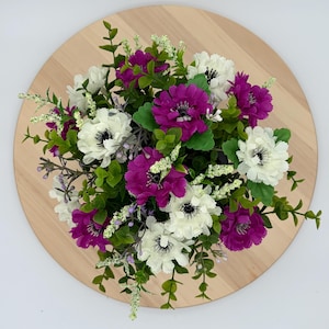 May include: A floral arrangement featuring a mix of vibrant purple and white anemone-style flowers, interspersed with small green leaves and delicate white filler sprigs, creating a dense, rounded bouquet with a balanced colour distribution.
