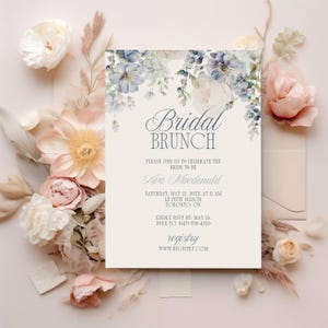 May include: A bridal brunch invitation with floral accents. The invitation features the text "Bridal Brunch" and details for Ava Macdonald's event. Soft pink and blue flowers surround the invitation, with additional floral elements.