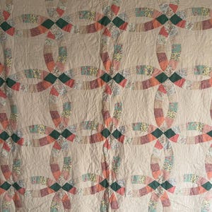May include: A quilt featuring a repeating double wedding ring pattern. The rings are constructed from small, multi-colored floral and geometric fabric patches in shades of pink, green, and yellow, set against a solid cream-colored background.