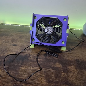 Könnte beinhalten: Ein lila und grüner Computerlüfter mit einem schwarzen Lüfterrad. Der Lüfter ist mit einem schwarzen USB 3.1-Kabel verbunden. Der Lüfter steht auf einer Holzoberfläche.