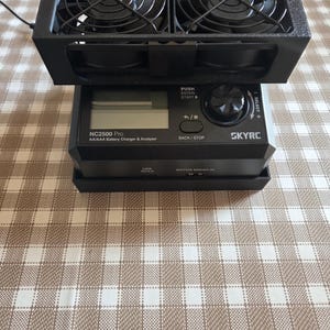 Könnte beinhalten: Ein schwarzes Batterieladegerät und -analysator mit dem Text "NC2500 Pro" und "SKYRC". Das Gerät hat ein digitales Display, Tasten und ein Kühlsystem mit Lüftern oben. Der Text "PUSH ENTER START" ist ebenfalls sichtbar.