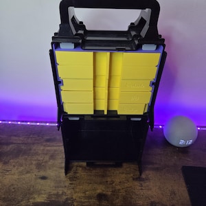 May include: Black and yellow tool organiser with a handle. The organiser has multiple yellow compartments and the text "Fastrack 3D Systems". The organiser is open, revealing the compartments.
