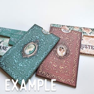 May include: Two rectangular paper card holders with pull tabs, one in teal and one in maroon, both featuring intricate filigree patterns, ornate oval frames containing portraits of women, and the word Pull printed on the top tab of each item.