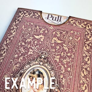 May include: A rectangular paper sleeve with a deep burgundy and gold ornate filigree pattern. A semi-circular tab at the top features the word Pull in dark script. A central oval frame contains a portrait of a person with light hair.