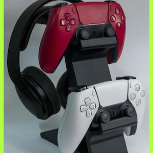 May include: A black stand holding a red and a white game controller, with a black headset resting on top. The controllers have a modern design with multiple buttons and a central touchpad. The stand is black and angled.