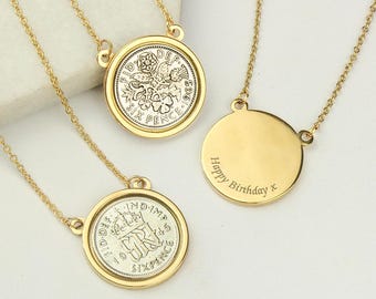 May include: Gold-toned necklaces with coin pendants. The coins are set in gold frames and feature intricate designs. One necklace has a blank, round pendant with "Happy Birthday x" engraved. The necklaces are displayed on a white surface.