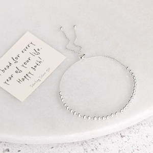 Op de afbeelding: Een zilveren verstelbare armband met kleine, ronde kralen. Een klein kaartje naast de armband luidt: "Een kraal voor elk jaar van je leven. Gelukkige 30e! Sterling Zilver 925."