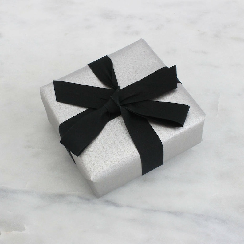 May include: A silver gift box with a black ribbon tied in a bow.
