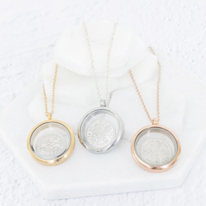 May include: Three coin locket necklaces in gold, silver, and rose gold. Each pendant has a clear glass front, displaying a detailed coin. The necklaces hang on fine chains, suitable for daily wear.