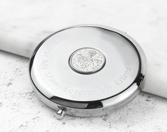 May include: A round, silver-colored compact mirror with a coin in the center. The mirror has the engraved text "First My Mum, Forever My Friend". The coin is a sixpence from 1963.