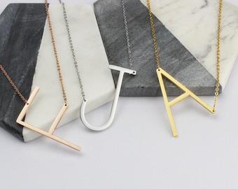 May include: Three necklaces featuring large, flat, capital letter pendants in rose gold, silver, and gold tones. Each pendant is attached to a delicate matching chain, showcasing the letters L, J, and A in a clean, modern, sans-serif typeface.