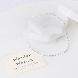 Puede incluir: Pulsera de plata con una cadena delicada y peque&ntilde;as cuentas de plata. La pulsera deletrea "Wonder Woman" en c&oacute;digo Morse. El texto en la tarjeta dice "Wonder Woman Morse Code by: Charlie Boots Sterling Silver $25".