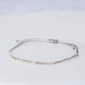 Puede incluir: Un brazalete de cuentas plateadas con un cord&oacute;n gris. El brazalete tiene una mezcla de cuentas redondas y cil&iacute;ndricas.