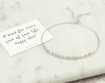 May include: A silver bracelet with small, round beads and an adjustable clasp. A card next to the bracelet reads "A bead for every year of your life. Happy 16th!" and "Sterling Silver 925."