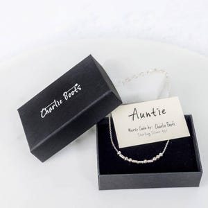 Könnte beinhalten: Eine schwarze Box mit den Worten "Charlie Boots" auf dem Deckel. In der Box befindet sich eine silberne Halskette mit einer Karte, auf der "Auntie" und "Morse Code by: Charlie Boots Sterling Silver 925" steht.