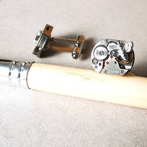 May include: A pair of silver cufflinks with a bee design. One cufflink features a bee on top of a watch mechanism. The other cufflink is a simple silver design.