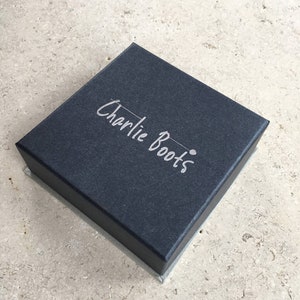 May include: A black square box with the words "Charlie Boots" embossed in silver lettering.