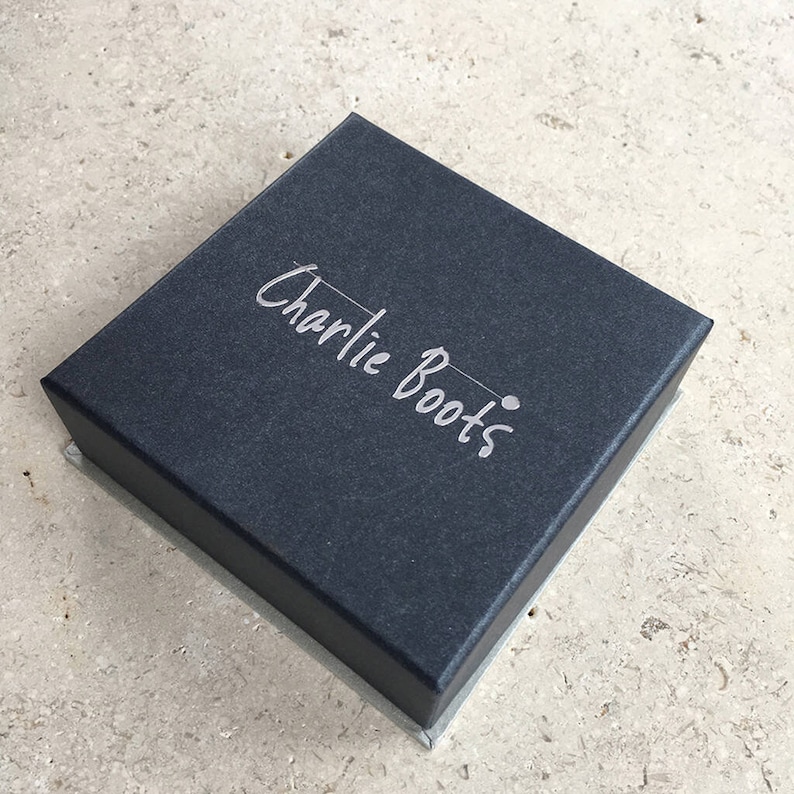 May include: A black square box with the words "Charlie Boots" embossed in silver lettering.