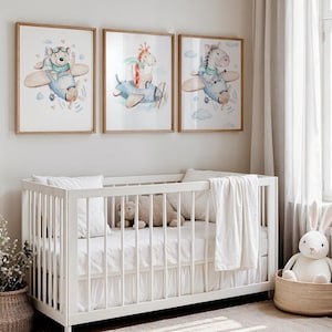 May include: Three framed watercolor prints of animals in vintage airplanes hang above a white crib. The prints feature a bear, giraffe, and zebra, each in a different plane. The nursery is decorated in neutral tones with a wicker basket and stuffed bunny.