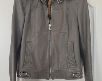 May include: A gray leather jacket with a zip-up front, collar, and buckle details. The jacket has a tailored fit and a leopard print lining. It is hanging on a black hanger.