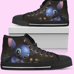 May include: High-top canvas sneakers featuring a blue cartoon character with large eyes and ears. The shoes have a black sole, laces, and toe cap. The background is dark with a hint of green.