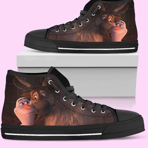 May include: High-top canvas sneakers featuring a cartoon image of Sven and Olaf from the movie Frozen. The shoes have a black toe cap, black laces, and a white stripe along the sole. The background is a light pink.