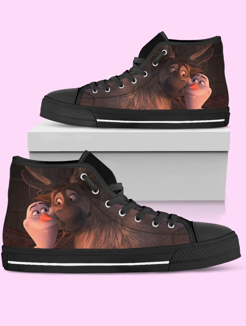 May include: High-top canvas sneakers featuring a cartoon image of Sven and Olaf from the movie Frozen. The shoes have a black toe cap, black laces, and a white stripe along the sole. The background is a light pink.
