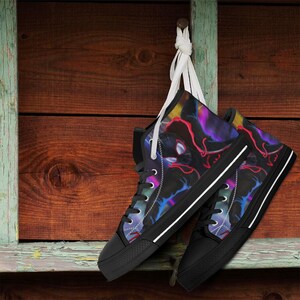 May include: A pair of high-top sneakers with a black base and a vibrant, colorful design featuring red, purple, and blue accents. The sneakers have black laces, a white stripe on the sole, and are hanging against a wooden background.