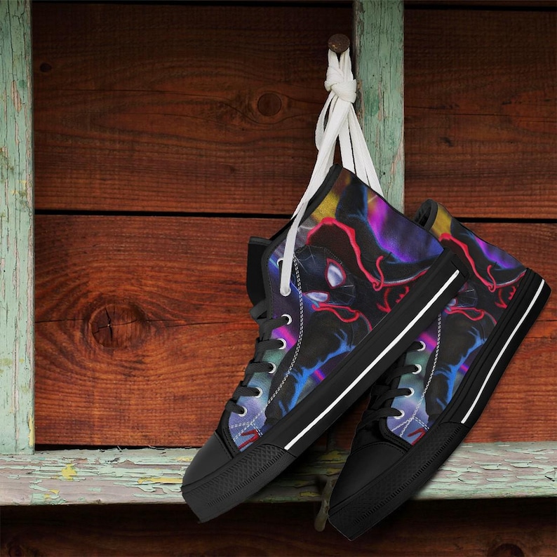 May include: A pair of high-top sneakers with a black base and a vibrant, colorful design featuring red, purple, and blue accents. The sneakers have black laces, a white stripe on the sole, and are hanging against a wooden background.