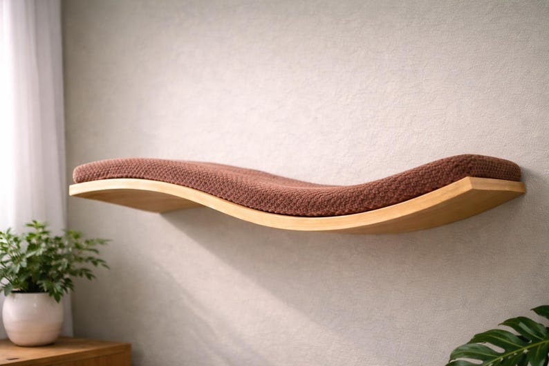 May include: A wooden cat shelf with a curved design, featuring a brown, textured cushion. The shelf is mounted on a light-colored wall, providing a comfortable and stylish resting spot for pets. The shelf is approximately 30 inches long.