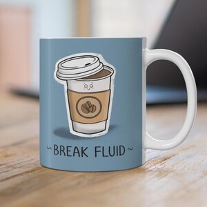 May include: A white ceramic coffee mug with a blue background. The mug features a cartoon illustration of a coffee cup with a smiling face and the text "BREAK FLUID". The coffee cup has a brown sleeve and a white lid.