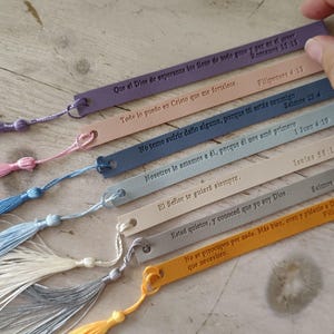 May include: A collection of colorful leather bookmarks with attached tassels. Each bookmark features embossed text in a script font, with a small hole at the top for the tassel. The bookmarks are in various colors, including purple, pink, and yellow.