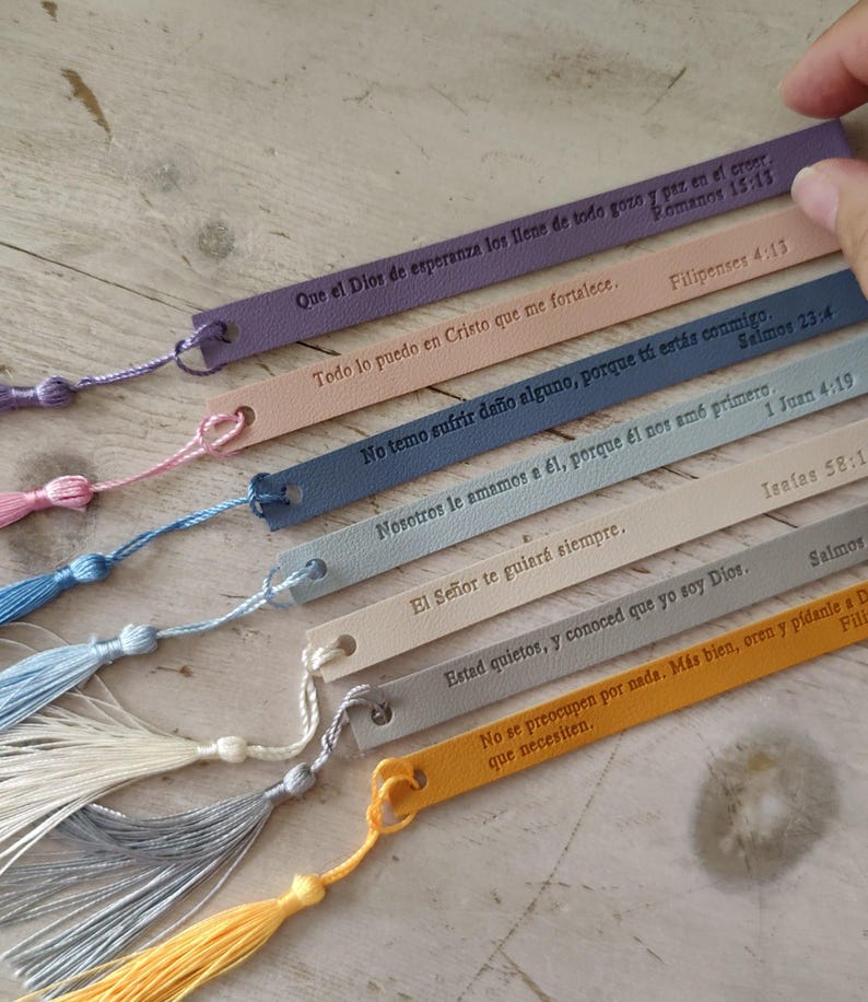 May include: A collection of colorful leather bookmarks with attached tassels. Each bookmark features embossed text in a script font, with a small hole at the top for the tassel. The bookmarks are in various colors, including purple, pink, and yellow.