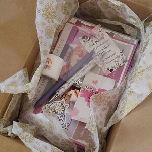 May include: A cardboard box filled with stationery items, including pens, stickers, and cards. The box contains a pen with the text "Be Strong And Courageous" and a sticker with the word "HOPE". The box is lined with tissue paper.