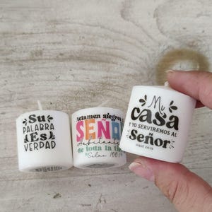May include: Three white votive candles with black text. One candle says "Su PALABRA ES VERDAD", another says "Aclamen alegres SE&Ntilde;OR Habitante de toda la tie #Salms 100", and the third says "Mi casa Y YO SERVIREMOS AL Se&ntilde;or".