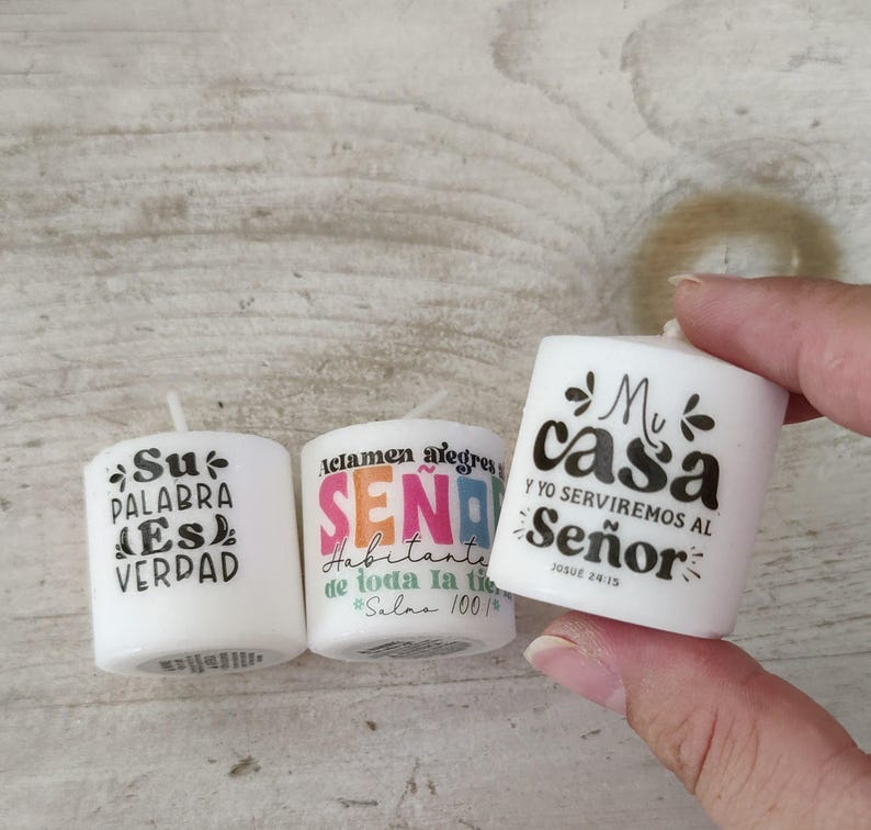 May include: Three white votive candles with black text. One candle says "Su PALABRA ES VERDAD", another says "Aclamen alegres SE&Ntilde;OR Habitante de toda la tie #Salms 100", and the third says "Mi casa Y YO SERVIREMOS AL Se&ntilde;or".