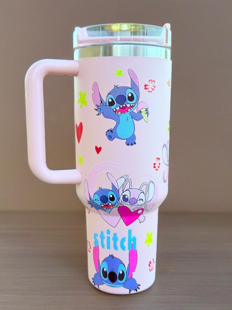 May include: A pink insulated travel mug decorated with Stitch from Lilo & Stitch. The mug has a pink handle and lid, with various images of Stitch and floral designs. The word "stitch" is written in blue and pink.
