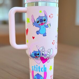 May include: A pink insulated travel mug featuring Stitch from Lilo & Stitch. The mug has a handle and a lid. Stitch is shown in different poses with hearts and flowers. The word "stitch" is written in blue and pink.